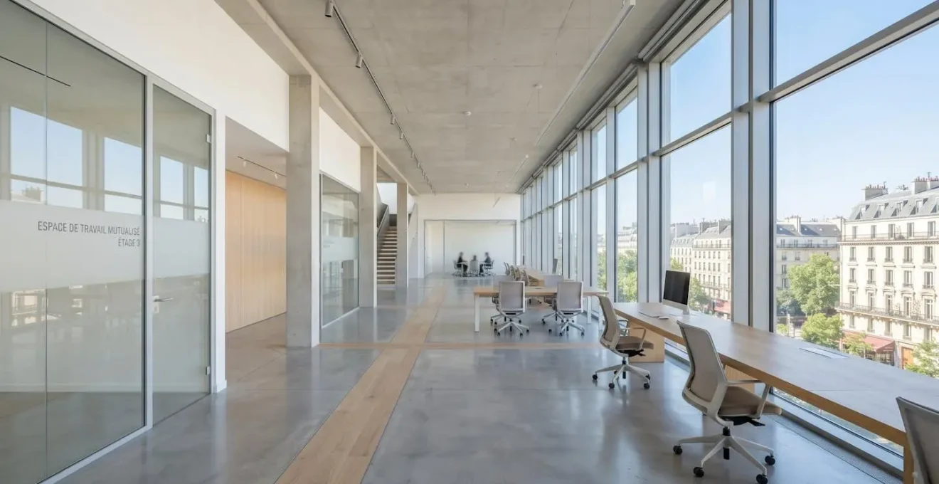 Espace de travail contemporain épuré avec grandes baies vitrées laissant entrer une lumière naturelle abondante, bureau vide au premier plan